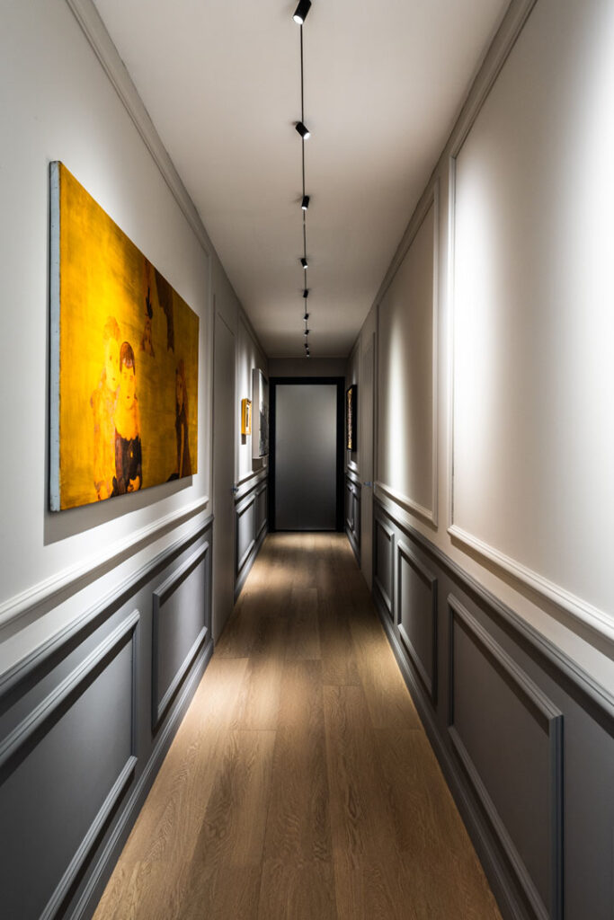 Corridoio con boiserie continua e opera d arte illuminata da binario magnetico