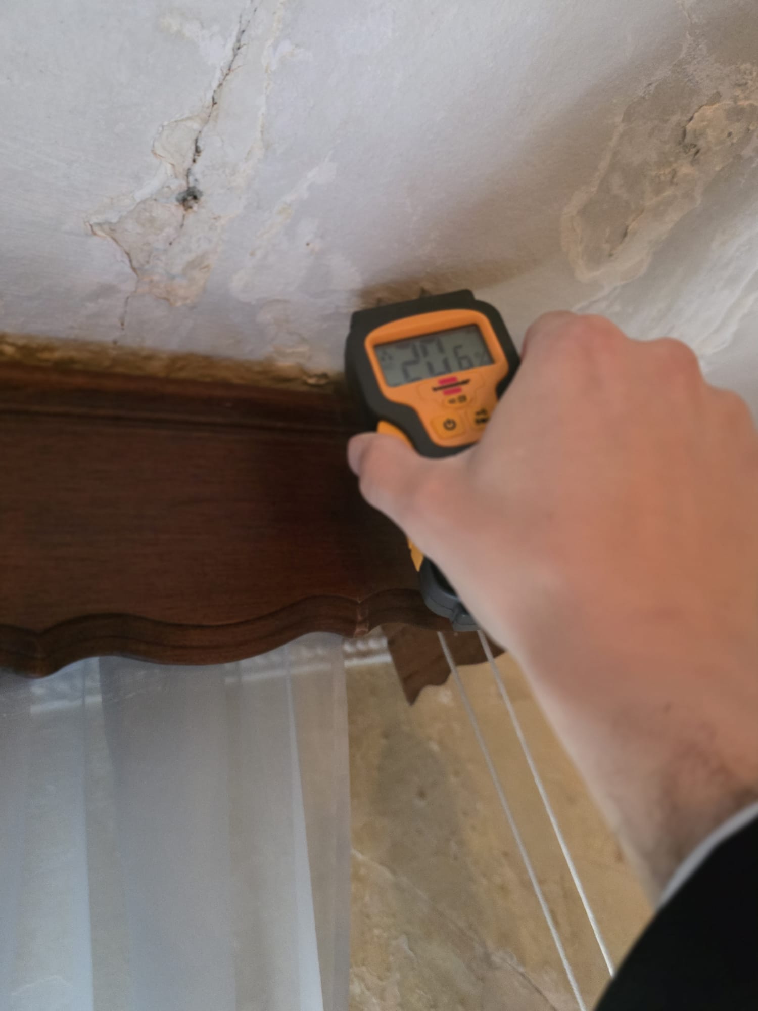Tecnico Archilife che misura il contenuto d'acqua con igrometro sull'angolo tra parete e soffitto, dove sono presenti muffa e crepe nell'intonaco