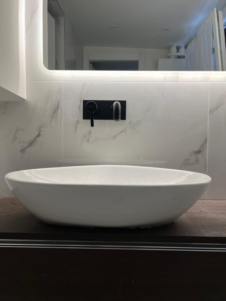 Bagno rifatto con lavabo da appoggio, miscelatore a parete nero e gres effetto marmo a tutta altezza