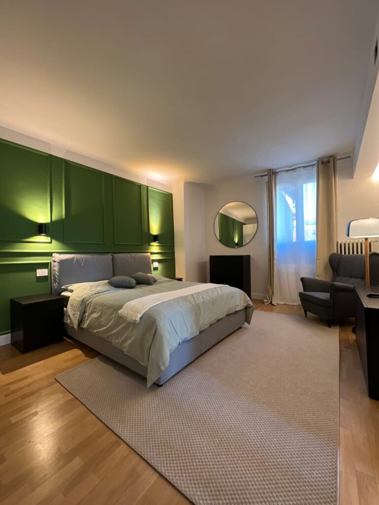 Camera da letto con boiserie verde a tutta altezza che sostituisce la testata del letto e applique a parete