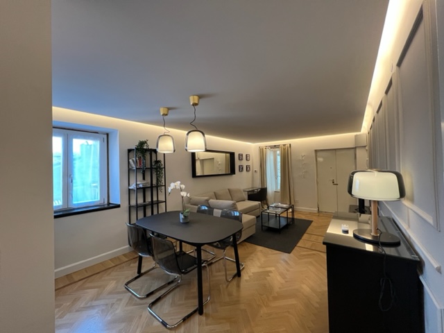 Zona pranzo del bilocale in via Pace a Brescia con tavolo nero, lampade a sospensione e parquet in rovere mantenuto