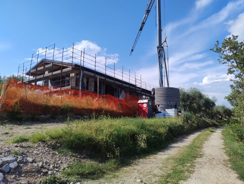 La villa in costruzione con ponteggio e gru, vista dal sentiero tra gli uliveti